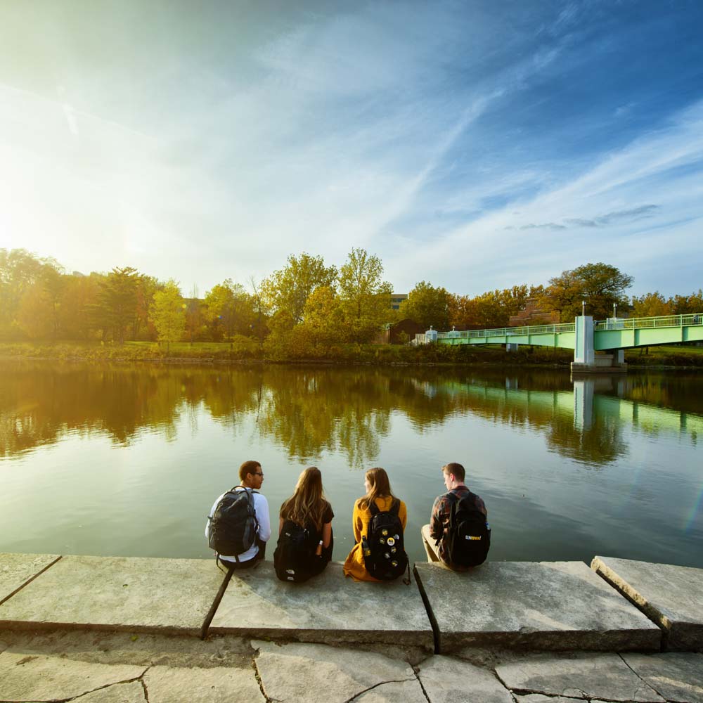 Four students sitting on dock along the Iowa River.