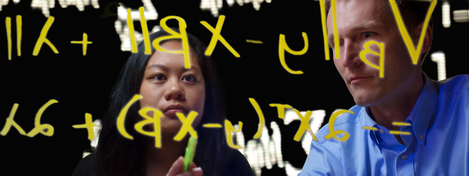 two people looking at mathematical equations written in marker on glass