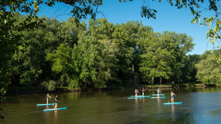 Students paddleboarding along the Iowa River.