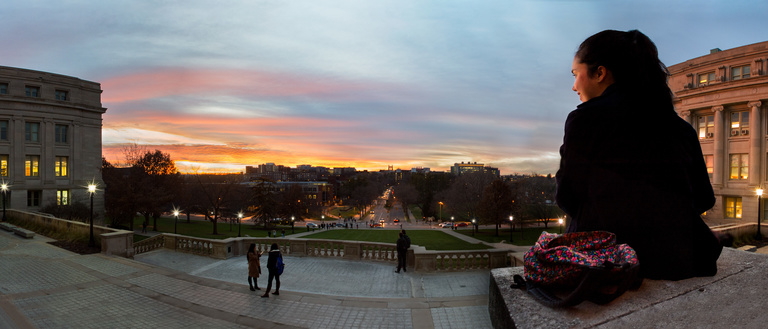 Student sits on Old Capitol steps overlooking the west part of the campus as the sun sets.