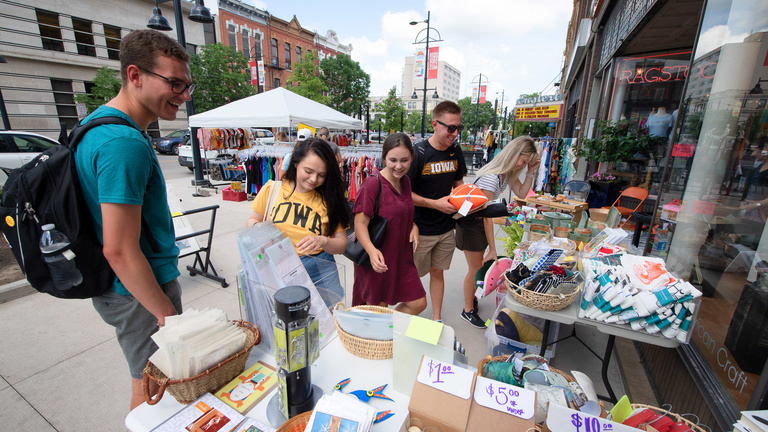 Four students looking at merchandise on a table outside in downtown Iowa City.