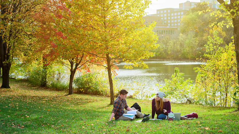 Two students studying under a tree along the Iowa River.