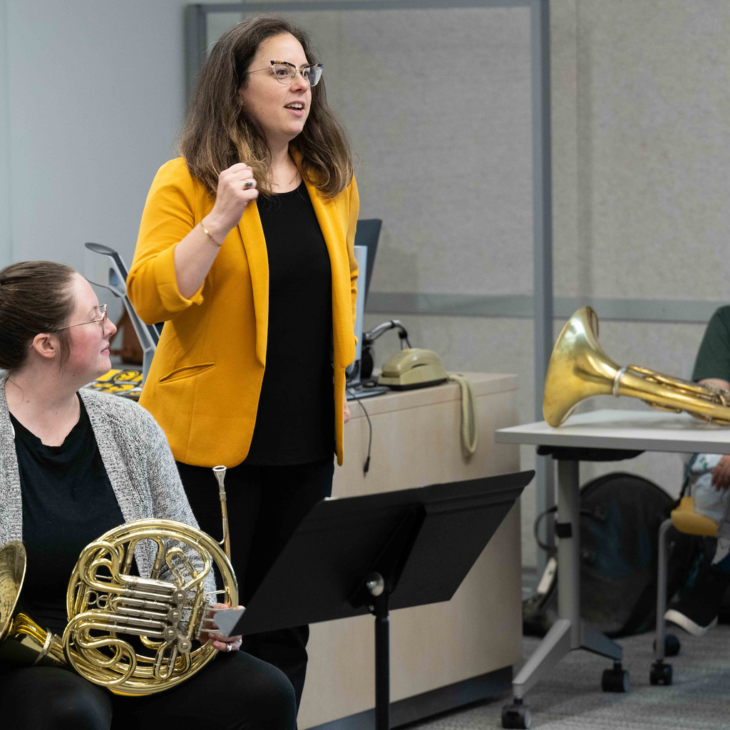 Teacher with yellow jacket talking with french horn in hand