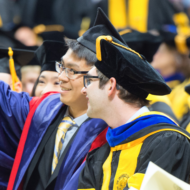 Two students take a selfie during graduate commencement.