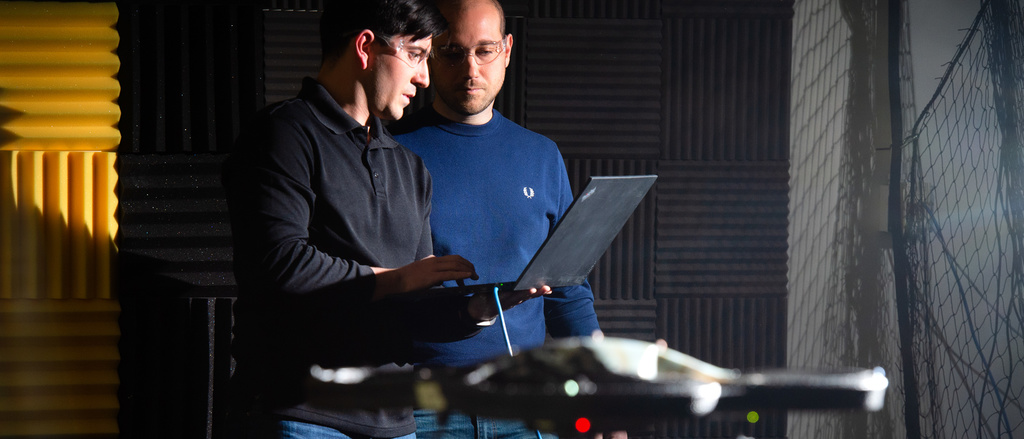 Two students work with a computer connected to a drone in flight.