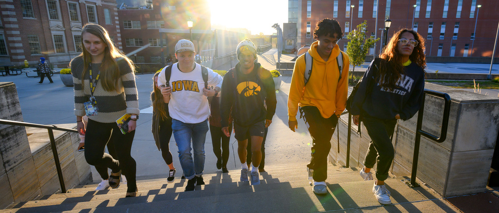 Alt="Six students walking up steps with sunset behind them."