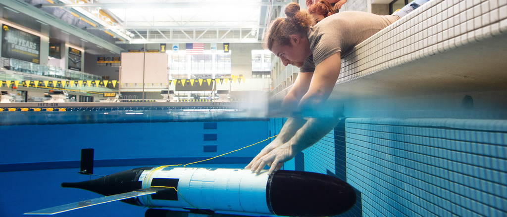 Student holding research glider under the water in a pool.
