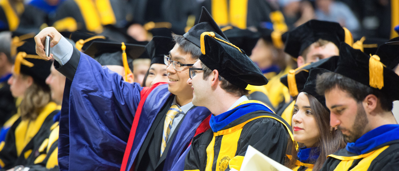 Two students take a selfie during graduate commencement.