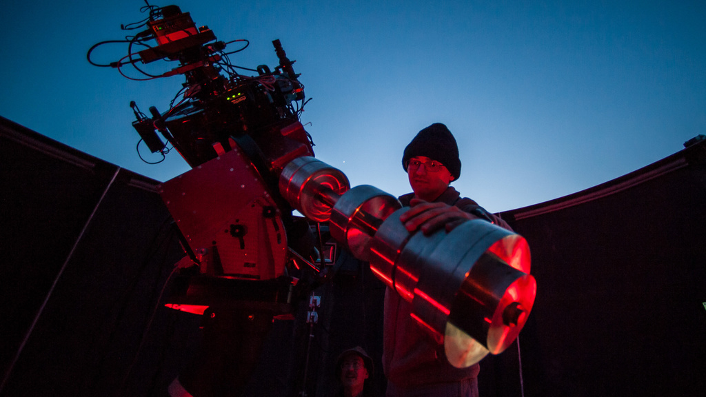Student adjusts telescope on rooftop observatory.
