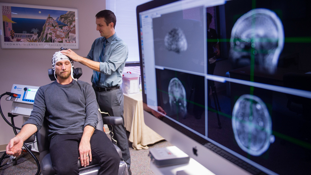 Doctor placing cords on research subject's head with scans on a monitor next to them.