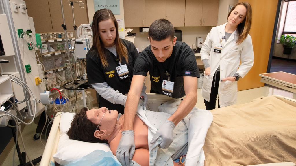 two nursing students practice techniques on artificial patient.