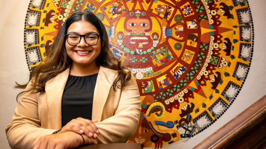 University of Iowa student Guadalupe De La Rosa standing at the bottom of a staircase with artwork behind her