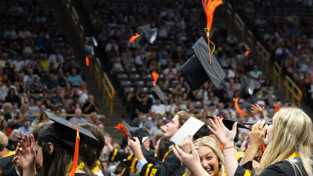 graduates throwing their caps in the air at a university of iowa college of engineering commencement ceremony