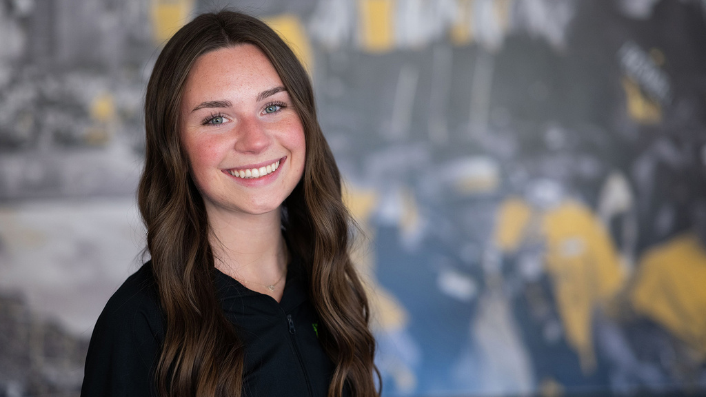 University of Iowa student Amelia Early stands in front of a black-and-gold themed wall that is in soft focus