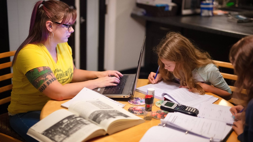 Woman sitting typing on a laptop with kids doing homework at the table