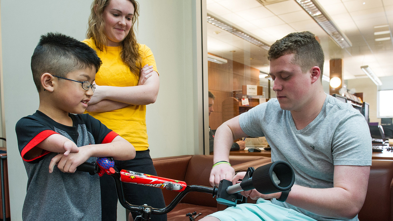 biomedical engineering students install a device on a bicycle that will help a boy with a partial limb better ride the cycle