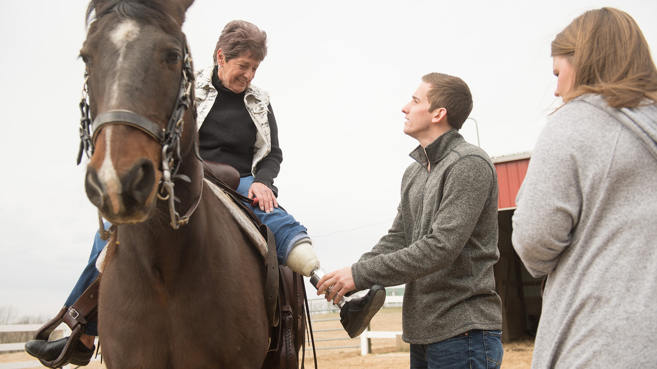 a man helps a woman on a horse with her prosthetic limb