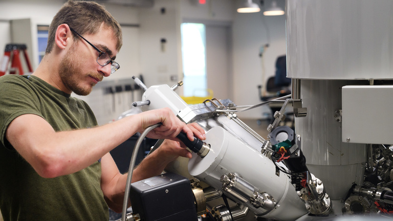 Student inserts a cord into micro fabrication research equipment.