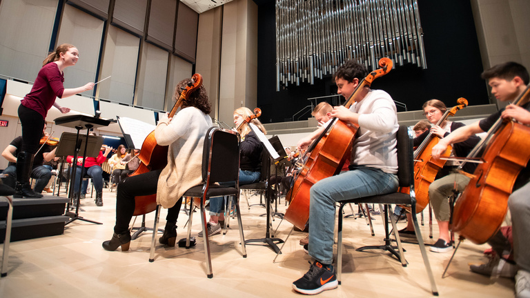 Student orchestra rehearses in an auditorium.