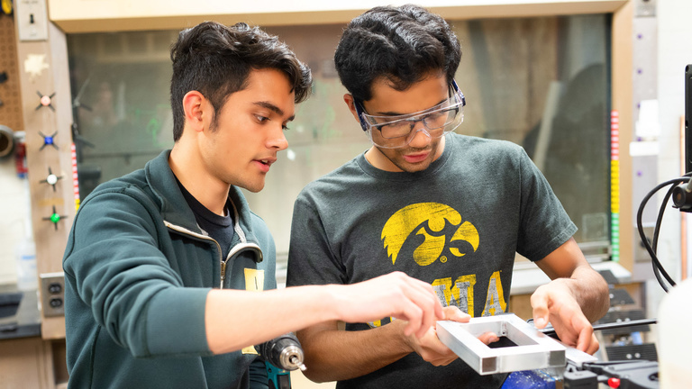 Two students work on robotics parts in a lab.