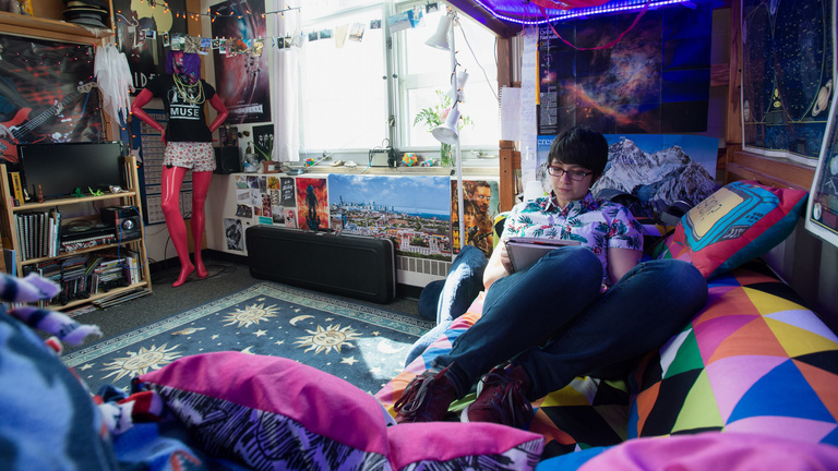 Woman sits on bed studying in dorm room.
