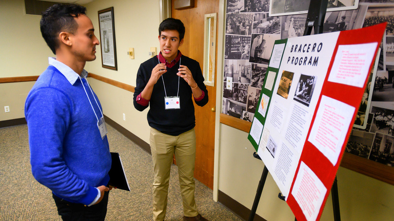 Two students talking in front of poster.